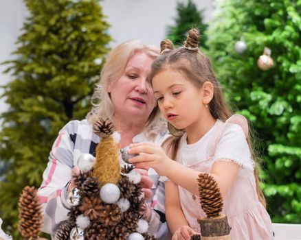 Elderly caucasian woman making pine cones decoration for christmas with two granddaughters.