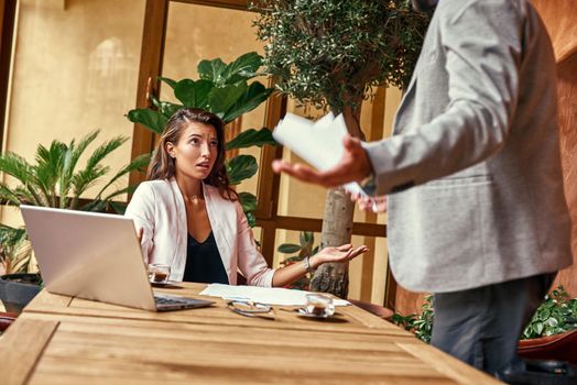 Business lunch. Woman sitting at table while man standing hands aside arguing irritated close-up