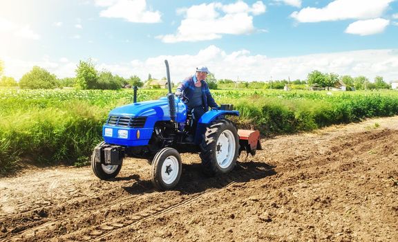 A farmer rides across the field on a tractor with a milling machine. Loosening surface, cultivating land for planting. Farming and agriculture. Work on the farm. Ground preparation for crop planting.
