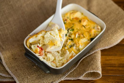 baked cauliflower with chicken fillet and vegetables topped with cheese in a ceramic mold