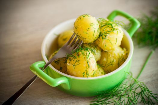 boiled early potatoes with butter and fresh dill in a bowl on a wooden table