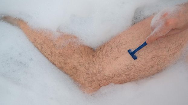 Funny picture of a man taking a relaxing bath and shaving his legs. Close-up of male feet in a bubble bath. Top view