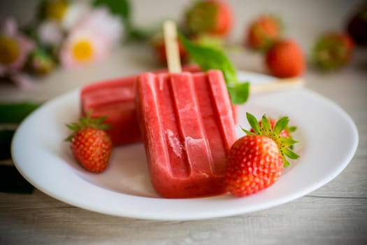 homemade strawberry ice cream on a stick made from fresh strawberries in a plate on a wooden table
