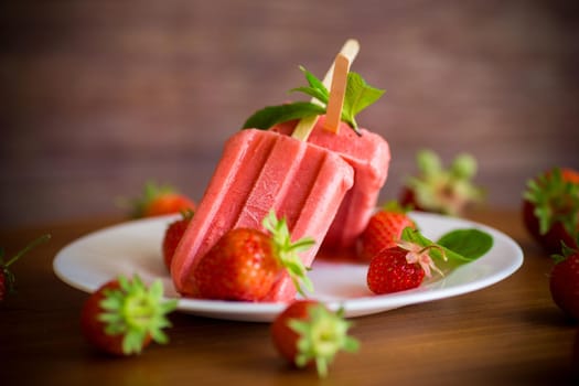 homemade strawberry ice cream on a stick made from fresh strawberries in a plate on a wooden table