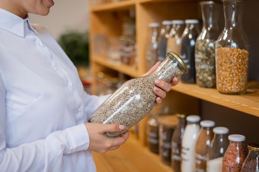 A woman is holding a jar of sunflower seeds. Selling bulk goods by weight in an eco store