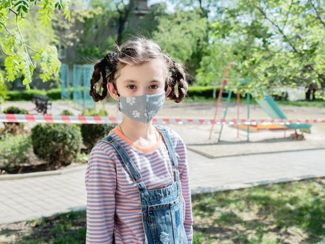 A little girl in a medical mask is not allowed to play in the playground during the coronavirus pandemic.