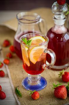 refreshing cool strawberry lemonade with lemon, ice and mint in a glass on a wooden table