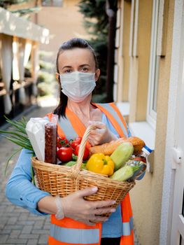 Portrait of a volunteer girl in a protective mask and medical gloves near the house of a man who is on self-isolation.