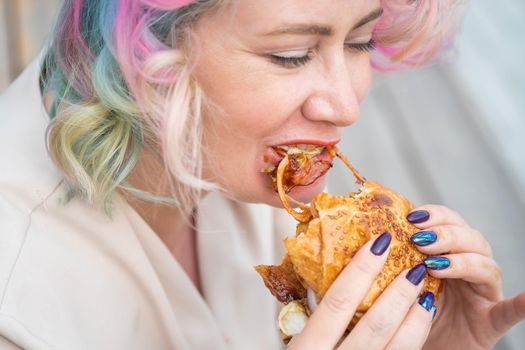 Caucasian woman with curly colored hair eating burger. Bad eating habits and love of fast food.