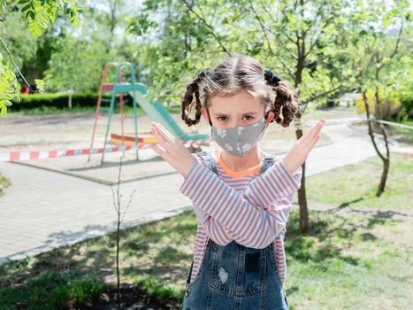 A little girl on the background of a fenced Playground forbids a gesture to violate the quarantine.