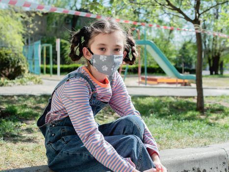 Sad little girl on the background of the closed Playground in the period of quarantine due to coronavirus infection