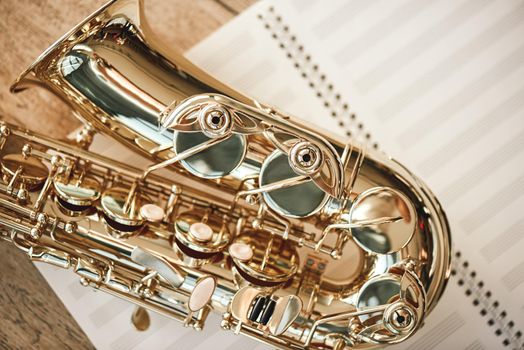 The joy of sax. Top view of beautiful shiny saxophone lying on sheets for music notes over wooden floor. Musical instruments. Music equipment.