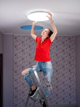 The girl hangs a ceiling lamp in the room.