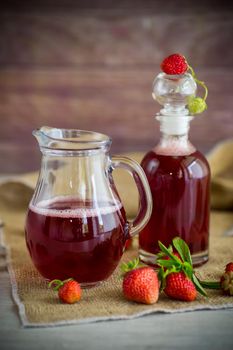 sweet cooked strawberry syrup in a glass decanter on a wooden table