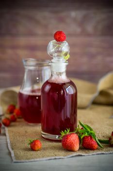 sweet cooked strawberry syrup in a glass decanter on a wooden table