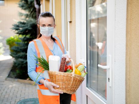 Portrait of a volunteer girl with a basket filled with food at the door of a person who is self-isolated during the coronavirus pandemic.