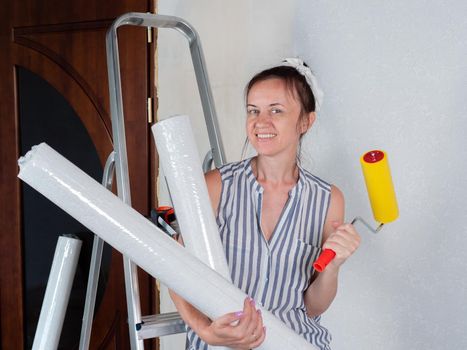 Portrait of a woman with rolls of Wallpaper near the stepladder in the room. Repairs in the apartment. Wallpapering in the room.