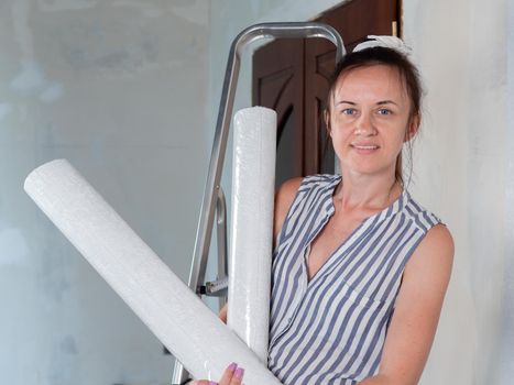 A happy woman holds rolls of new Wallpaper in her hands. Repairs in the apartment. Wallpapering.