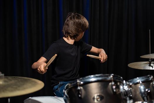 The boy learns to play the drums in the studio on a black background. Music school student.
