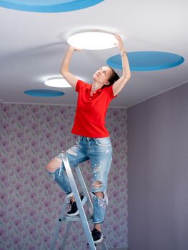 The girl hangs a ceiling lamp in the room.