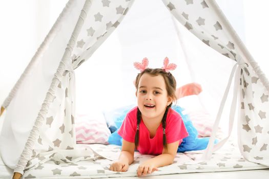 A little girl sits in a wigwam with pillows