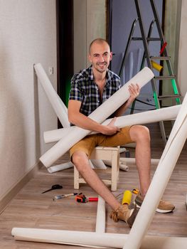 A man is smiling sitting on a bench with rolls of Wallpaper in his hands.