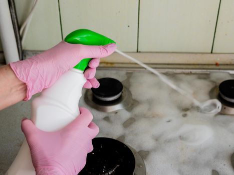 Close up of housewife hands in protective rubber gloves holding a sponge and spray and clean gas cooker.