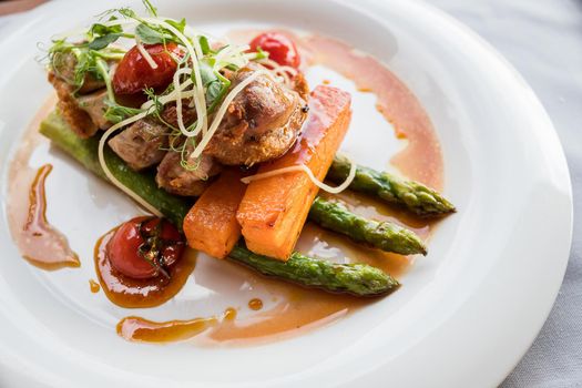 Roasted duck in slices with thyme in port wine sauce, served with cherry tomatoes, sliced potatoes, carrots and asparagus.