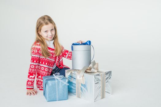 Pretty little girl wearing Christmas deer horns sitting isolated , holding stack of present boxes