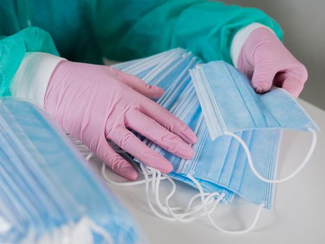 Close-up of a gloved woman counting blue masks at a table.