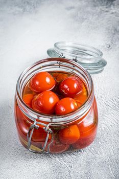 Pickled cherry tomatoes in a glass jar. White background. Top view.