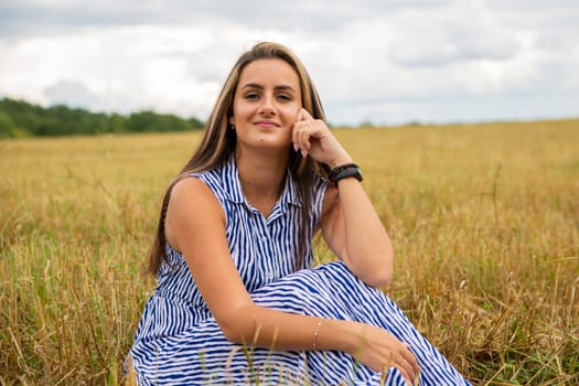 beautiful swarthy young woman sits in a meadow on a sunny day and enjoys the summer weather and wind.