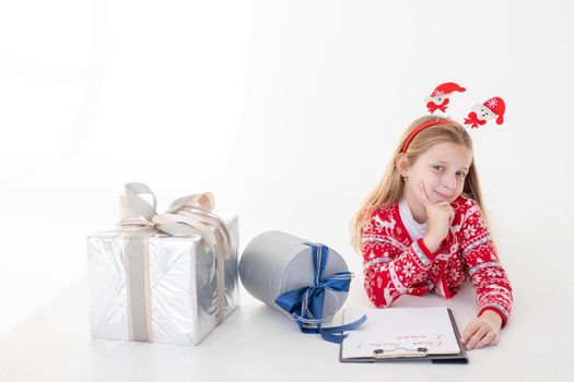 Thoughtful little girl in Santa hat writes letter to Santa Claus near christmas tree