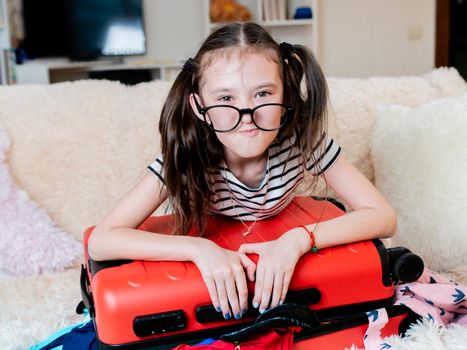 A little girl has Packed too many things on vacation, and can't close the red suitcase.