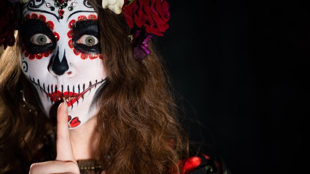 Woman in santa muerte makeup on a black background. Girl wearing traditional mexican holy death costume for halloween. Copy space.