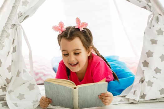 Portrait of pretty little girl reading book in cozy living room at home