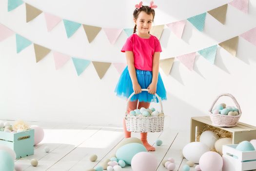 Getting ready to Easter. Lovely little girl holding an Easter egg and smiling with decoration in the background