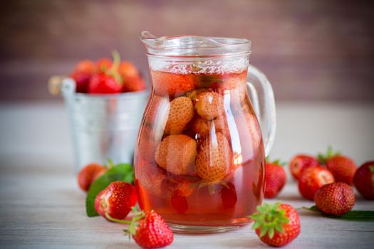 Sweet refreshing berry compote of ripe strawberries in a decanter on a wooden table