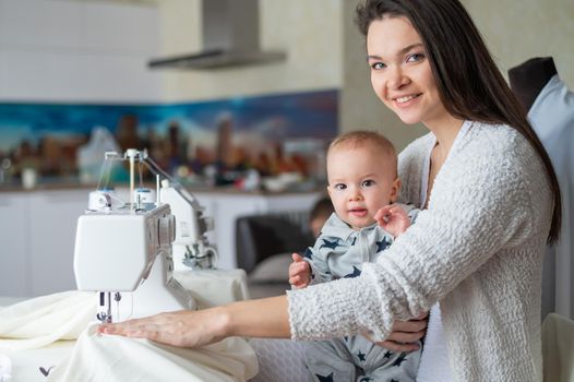 Young caucasian woman sews at home with a small child.