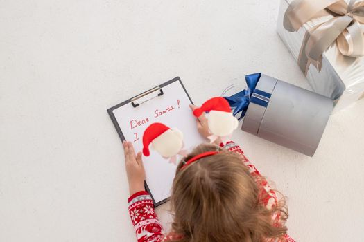 Dear Santa letter, Christmas card. Cute young girl wearing deer horns, holding a pen and writing on a white sheet