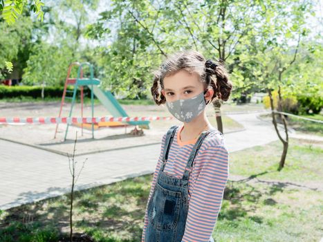 A little girl in a medical mask is not allowed to play in the playground during the coronavirus pandemic