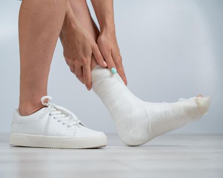 Close-up of female legs with plaster cast. A woman with a broken leg sits on a chair.