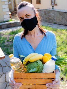 A woman in a protective medical mask with a food kit in a wicker basket for the poor.