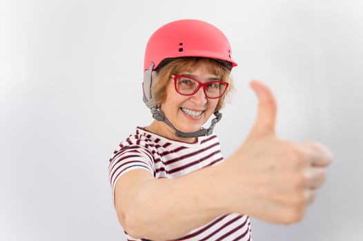 Elderly woman in ski helmet showing thumb up on white background
