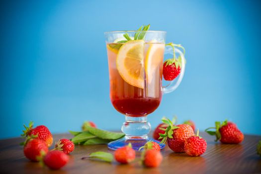 refreshing cool strawberry lemonade with lemon, ice and mint in a glass on a wooden table