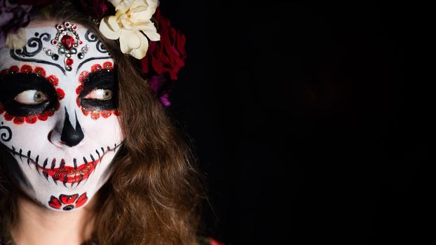Woman in santa muerte makeup on a black background. Girl wearing traditional mexican holy death costume for halloween. Copy space.