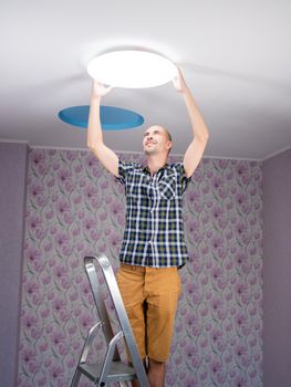 A man with a stepladder sets the ceiling lamp in the room.