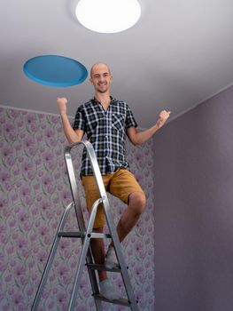 A happy man on a stepladder is happy that he has installed an led light on the ceiling.