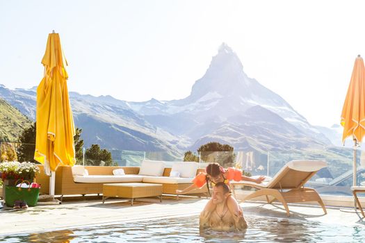 Family In Swimming Pool In Mountains. Beautiful outdoor scene in Swiss Alps, Switzerland, Europe.