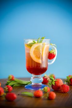 refreshing cool strawberry lemonade with lemon, ice and mint in a glass on a wooden table